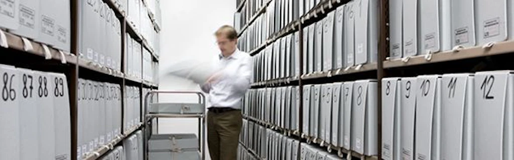 A man is standing in a storeroom full of archive boxes